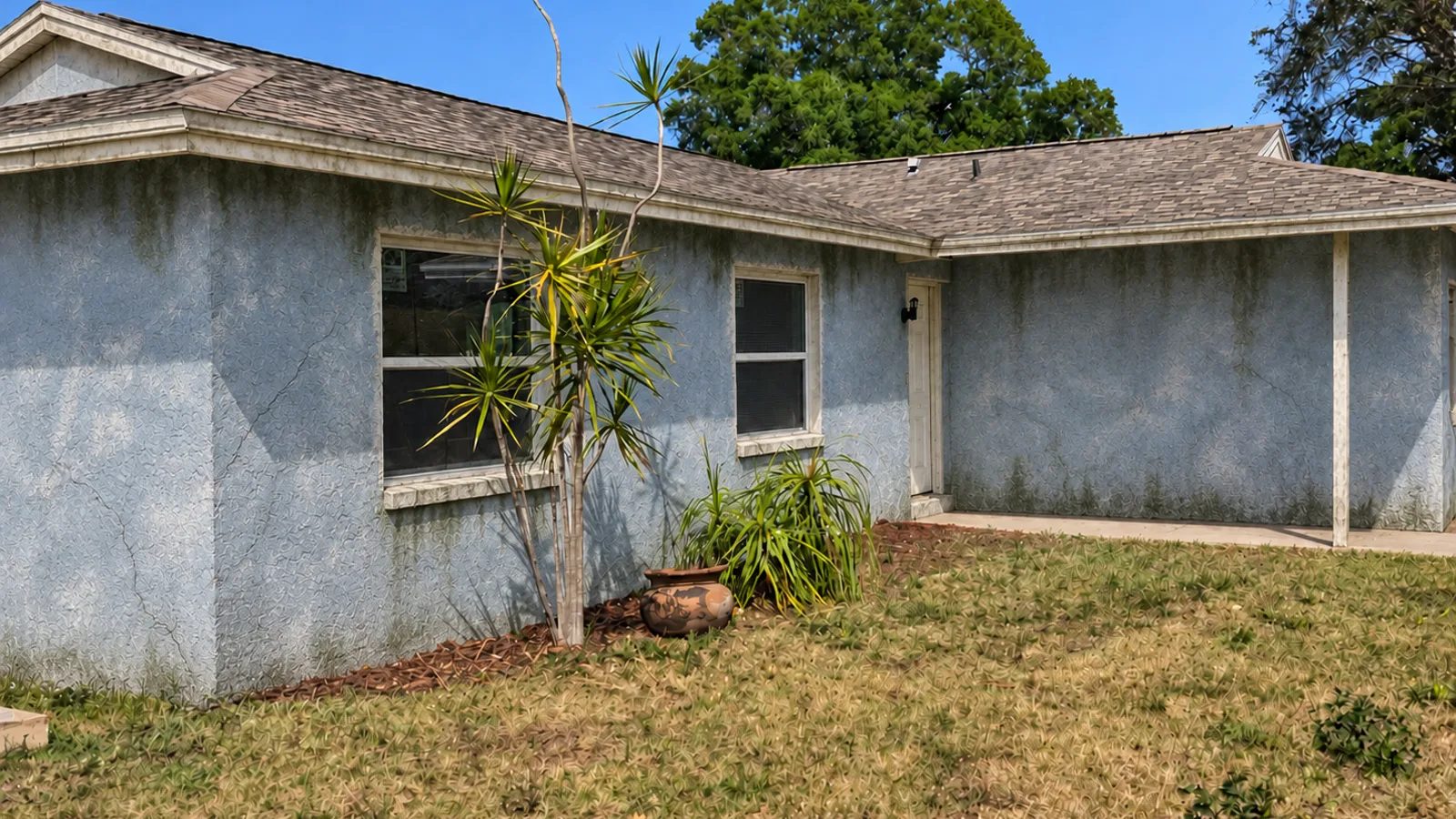 Single story Florida block home with chalky grey stucco and mildew streaks before painting